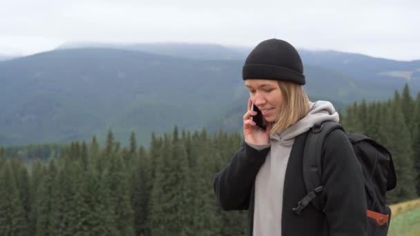 Una joven turista se para en la cima de la montaña y hace una llamada en su teléfono celular. espacio de copia. — Vídeos de Stock