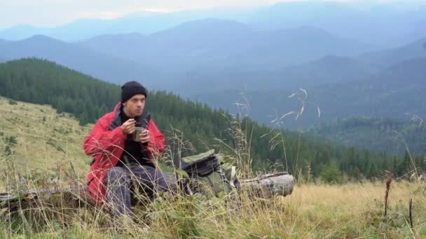 Un turista masculino come fideos instantáneos durante un alto. Disfrutando de hermosas vistas de la cordillera. En una camisa a cuadros. Temprano. Concepto de viajes y turismo. — Vídeos de Stock