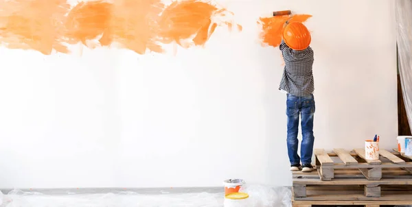 apartment renovation. Back view of a boy paints the wall with orange paint roller. The child helps to make repairs. Room renovation concept. Child interior wall.banner