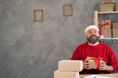 Noel Baba şapkalı küçük bir işletme sahibi evinde hediyesiyle oturuyor. Noel indirimi ve eşya satıcısı. Yeni yıl için iş konsepti. Metin için yer