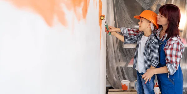 Home repairs. Mom helping her son paint the wall with a roller. The boy paints the wall of the apartment. New house renovation concept. — Stock Photo, Image