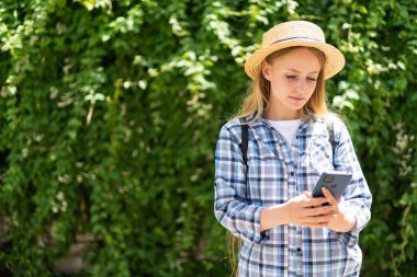 Şapkalı turist kız telefonu Avrupa 'da bir şehirde kalacak yer aramak için kullanıyor. Sosyal ağ için teknoloji ve cep telefonları