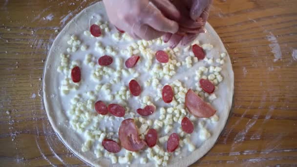 Vaření pizzy. Ženské ruce dávají kousky párku na syrovou pizzu se salámem a sýrem. Tenká italská pizza s klobásou v pizzerii. — Stock video