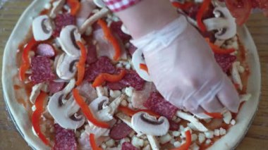 Pizaiolla pizzacıda mantarlı, salamlı ve pepperonili pizza yapar. Fırıncı elleri ve çiğ pizza..