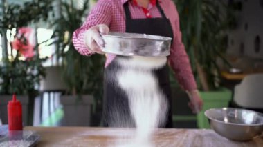 Kadın fırıncı pizzacı pizzacıdaki ahşap mutfak masasında süzgeçten çıkan un püresi hazırlıyor. Ön planda un serpintisi. kafe biçimi.