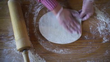 Pizza hamurunu yuvarlayan bir aşçının elleri masanın üstünde yuvarlanan bir raptiye, üst manzara. Pizza ya da kafede İtalyan pizzası pişirmek. Yiyecek.