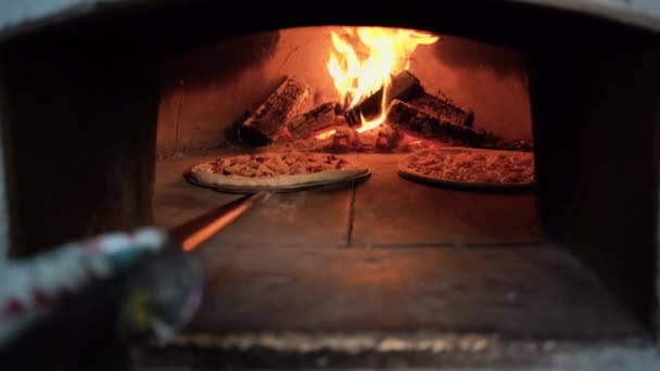 Cozinhar pizza tradicional em um forno a lenha aberto. As mãos de padeiros põem a pizza crua em um forno de tijolo. Pizza italiana — Vídeo de Stock