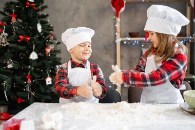 Mutlu fırıncılar mutfakta hamur yoğuruyor. Erkek ve kız kardeş masada Noel pastası için para kazanıyorlar. Bir erkek ve bir kız ekmek hazırlıyorlar.