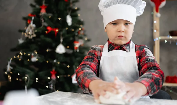 Porträt eines kleinen Bäckers in Uniform, der Brotteig backt. Junge bereitet Plätzchen oder Lebkuchen für Weihnachten zu. Das Kind macht Pizzateig. — Stockfoto