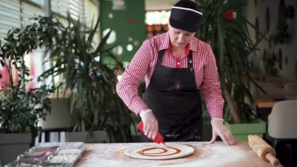 Detailní záběr kuchaře, jak nalévá rajčatovou omáčku na těsto na pizzu. Tradiční italská pizza restaurace. Pizzerie pekař připravuje pizzu s tradiční kečup omáčkou. — Stock video