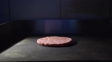 Buharla kızartılmış yuvarlak çiğ hamburger pirzolası. Çocuk menüsü için hamburger pişiriyorum. Bir fast food kafede hamburger bifteği. Siyah gıda geçmişi.