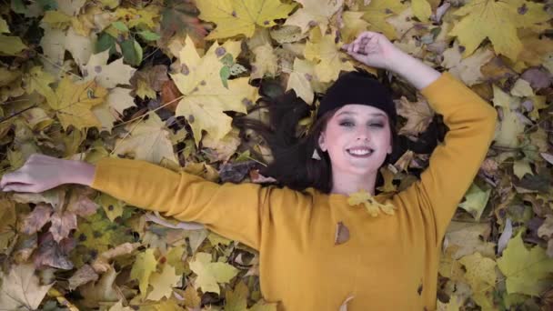 Parkta sarı sonbahar yapraklarının üzerinde uzanan güzel kız. Dinlenme ve ekim ayında ormanda yürüyüş. Sonbahar konsepti. — Stok video