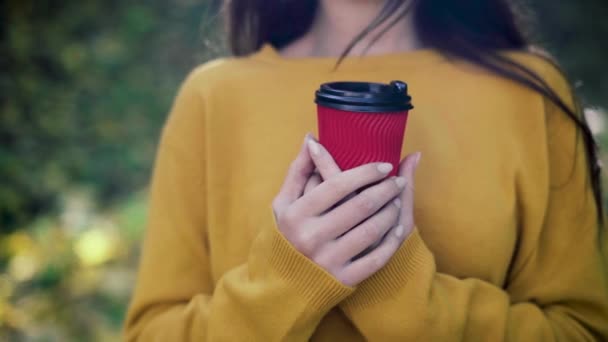 Ragazza in un parco autunnale con un bicchiere di caffè espresso caldo mattutino. E 'ora di riscaldarsi. Passeggiata nella foresta e relax autunnale. Caffè da asporto concetto. — Video Stock