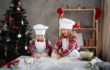 İki çocuk birlikte hamuru yoğuruyor, erkek ve kız kardeşler Noel kurabiyeleri yapıyor, mutfakta pişiriyor. Uzayı kopyala Neşeli arkaplan.