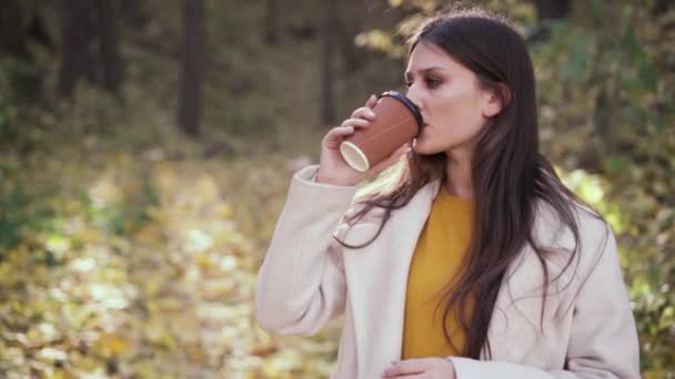 Горячий утренний кофе в осеннем лесу, девушка в стильном пальто, пьющая напиток, гуляющая по парку, приятный отдых осенью на природе. — стоковое видео