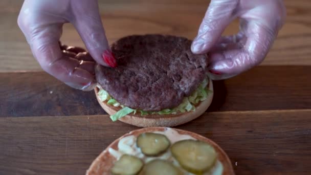 Процес приготування гамбургерів, жіночі руки готують бургер, кладуть котлети з яловичини, овочі в бургер, бургер швидкого харчування на дерев'яний стіл . — стокове відео