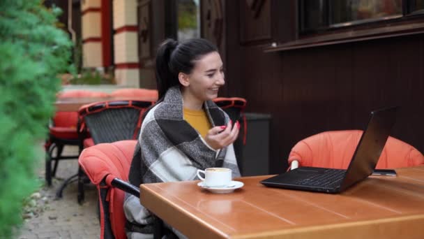 Verdadeira empresária trabalhando remotamente com um laptop no outono em um café de rua, ouvindo um webinar de rede, uma garota usando a Internet 5G em um restaurante — Vídeo de Stock