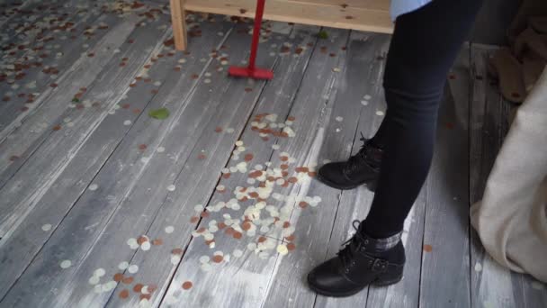 La señora de la limpieza en tacones altos limpia la casa después de una fiesta. Barrer el suelo con confeti con una escoba. Primer plano de las piernas femeninas. Servicios de limpieza. — Vídeo de stock