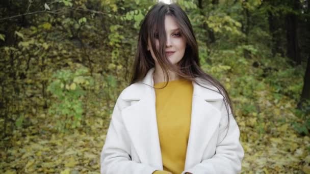 Idea autunnale. Sorriso fiducioso di una giovane ragazza in autunno nel parco sullo sfondo di foglie gialle cadute con la luce del sole. — Video Stock
