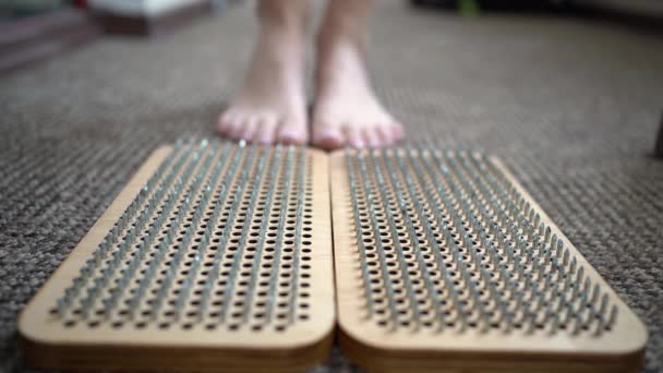 Woman stepping on wooden board with sharp metal nails, sadhu yoga board, foot relaxation, acuupuncture practice. — Stock Video