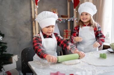 İki çocuk evde, mutfakta noel kurabiyelerinin üzerinde hamuru yuvarlıyor. Erkek ve kız kardeş kurabiye veya zencefilli ekmek yapıyor. Noel konsepti..