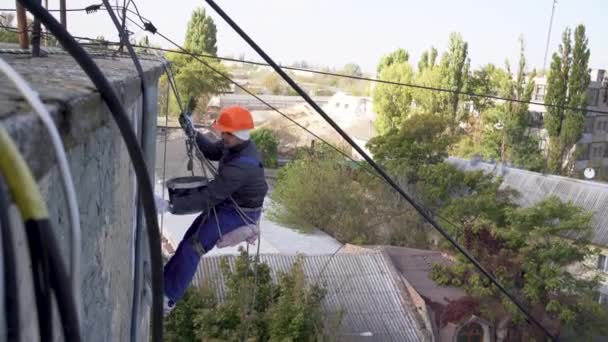 Side view of a Caucasian man hanging on a rope and plastering a multi-storey building. high-rise repair work. — Stock Video