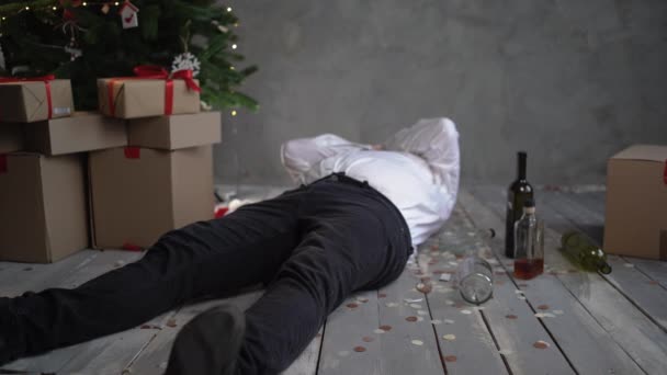 A drunken, bearded bald man wakes up in the morning after a corporate party on Christmas or New Years, picks up a bottle of wine under the tree and gets hungover. — Stock Video
