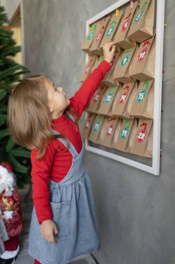 El yapımı Noel takvimi. Kız, duvardan küçük bir hediye alıyor. Profil görüşü, Noel geleneği için çocuk el sanatları..