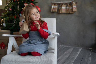 Koltuğunda Noel hediyesi olan bir kızın portresi, el sanatları paketlerinden gelen bir takvim, bir Noel ağacı ve arka planda hediye kutuları. Mutlu Noeller..