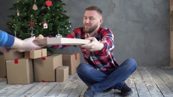 Entrega de comida, el mensajero de la pizza de Navidad le da una caja a un hombre barbudo, pidiendo comida a casa, un hombre de negocios solitario en el árbol de Navidad con pizza. Año Nuevo pizza entrega — Vídeo de stock
