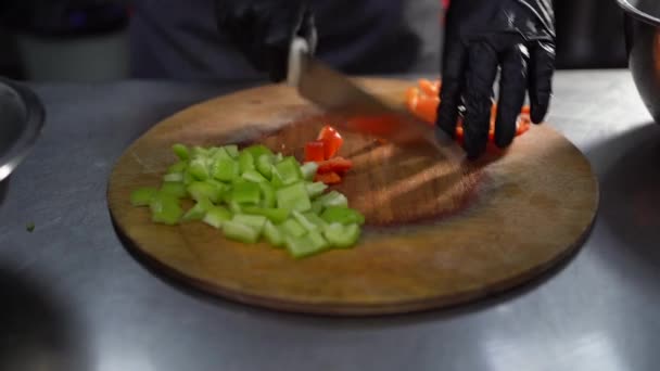 Cocinar comida en un restaurante, chef cortar pimiento rojo en una tabla de madera, cortar verduras con un cuchillo en una ensalada, fondo oscuro. — Vídeo de stock