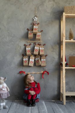 Mutlu kız duvardaki takvime bakıyor odada yerde oturuyor, el yapımı Noel dekoru, yatay manzara, çocuk şenlik hayranı konsepti