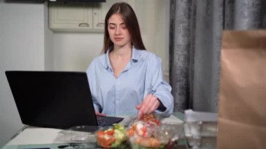 Kafkasyalı bir kadın akşamları evde tek başına dizüstü bilgisayar başında oturuyor ve çalışıyor. Tek kullanımlık sofra takımından plastik çatalla yemek yiyor. Paket servis konsepti..