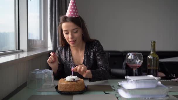 Een vrolijke mooie blanke vrouw met een feestelijke pet steekt een kaars in de taart voor haar verjaardag steekt het aan met een lucifer en doet een wens. — Stockvideo