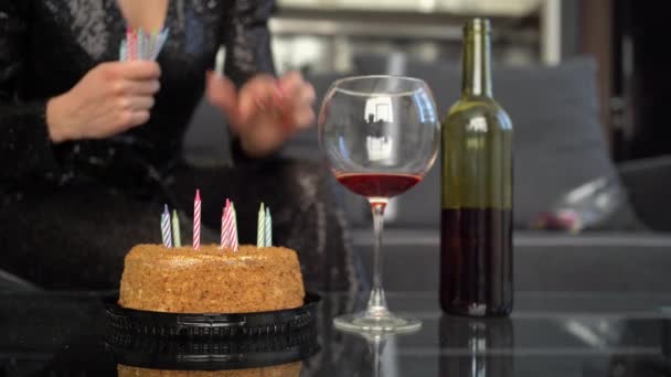 Close-up de mãos femininas inserir velas em um bolo de aniversário festivo. Uma garrafa de vinho e um copo estão sobre a mesa. preparação conceito para o aniversário do feriado. — Vídeo de Stock