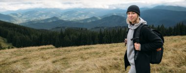 Ovada duran kız yürüyüşçü, kameraya bak, doğadaki turist macerası, dağlardaki arka plan, dağlık arazi ve özgürlük, seyahat ve dağ turizmi konsepti, afiş