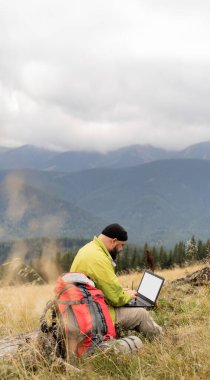 Diz üstü bilgisayarı olan beyaz sakallı bir adam vadinin güzel manzaralı dağdaki bir ağacın tepesinde oturuyor. Geniş bant hücre ağı kapsama alanı. 6G mi? Serbest çalışan biri uzaktan çalışıyor. Boşluğu kopyala