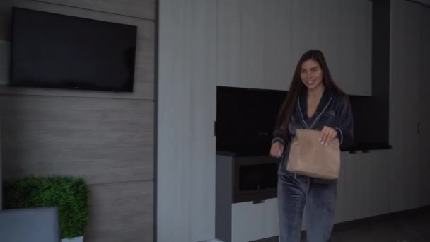 O femeie caucaziană fericită acasă poartă o pungă de hârtie cu mâncare. Un animal de companie Spitz păros aleargă în jurul camerei lângă amantă. în — Videoclip de stoc