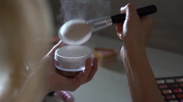 Pincel de maquiagem com uma explosão de pó bege. Close-up de mãos femininas que reúnem o pó em uma escova. — Vídeo de Stock