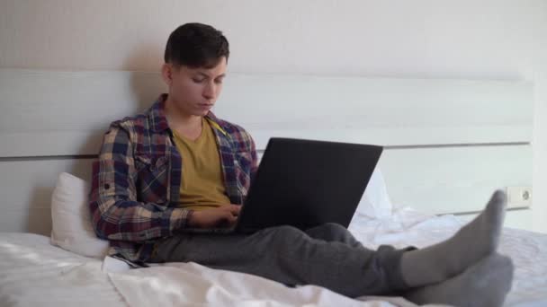 Un giovane caucasico è disteso a casa sul divano nel pomeriggio in abiti casual e lavorando sul suo computer portatile. Felice concetto di lavoratore remoto. — Video Stock