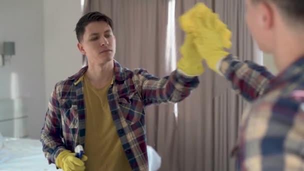 House cleaning. Caucasian man in casual clothes cleans the mirror from dust and dirt using spray and a yellow napkin. Rubber gloves on hands. — Stock Video