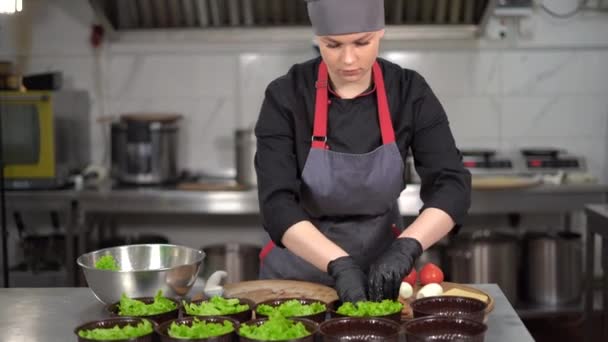 Entrega de comida o comida para llevar. Mujer joven chef en ropa especial pone hojas de lechuga en cajas de almuerzo desechables. — Vídeos de Stock
