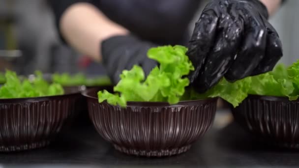 Makanan sudah siap untuk diantar. Di restoran, koki menyiapkan makanan dan menyiapkannya dalam kotak makan siang sekali pakai. Close-up of hands in gloves put a leaf of lettuce. — Stok Video