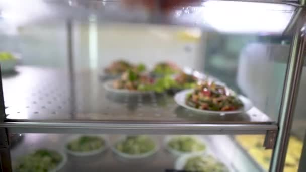 Zelfbediening eten met salades op de food service lijn of in de eetkamer tentoongesteld in de koelkast. mannelijke hand neemt een bord voedsel. — Stockvideo