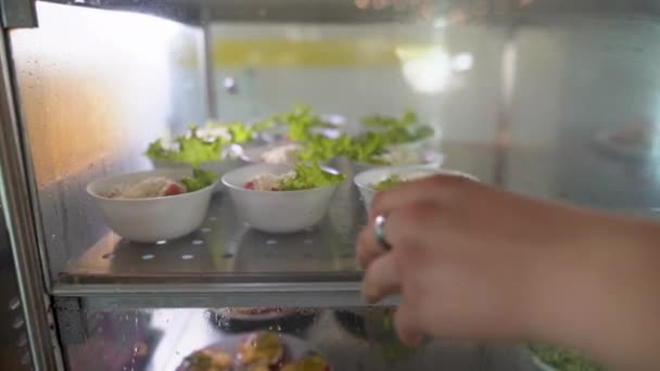 Zelfbediening eten met salades op de food service lijn of in de eetkamer tentoongesteld in de koelkast. mannelijke hand neemt een bord voedsel. — Stockvideo