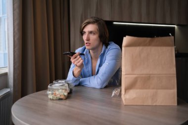 Sesli asistanı olan genç bir adam mutfağa yemek sipariş ediyor, yemekleri götürüyor sağlıklı öğle yemekleri yiyor, karantinada sağlıklı besleniyor, yemek siparişi veriyor.