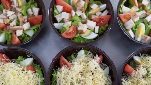 Na mesa há várias placas descartáveis com salada de dieta fitness. As mãos femininas põem o queijo ralado em cima. conceito de entrega de comida e mercearia. — Vídeo de Stock