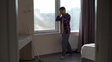 Kafkasyalı adam kafasına kulaklık takar ve daireyi temizlemeye başlar. Dans eden adam odayı paspasla yıkıyor..