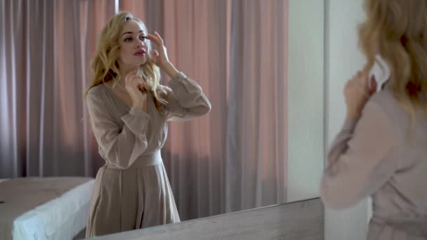 Mladá krásná běloška sama stojí v blízkosti zrcadla doma a obdivovat. — Stock video