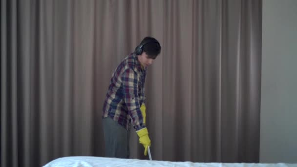 Biały mężczyzna ze słuchawkami na głowie sprząta dom. Tańczący facet myje podłogę w pokoju mopem jak gitara.. — Wideo stockowe